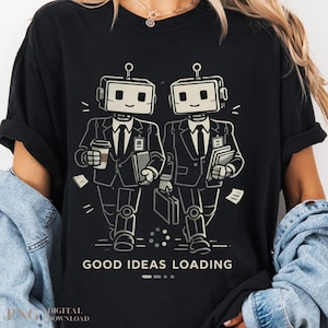 May include: A black t-shirt featuring a graphic of two robots dressed in business suits, ties, and ID badges. One robot holds a coffee cup and a book, while the other carries a briefcase and books. The text GOOD IDEAS LOADING is printed below.