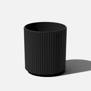 May include: A matte black cylindrical planter featuring a vertical ribbed texture along the exterior surface. The container has a consistent dark finish and a simple, open top design with a slightly recessed base, creating a clean and uniform appearance.