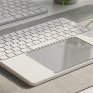 Puede incluir: Un teclado inalámbrico blanco que cuenta con un panel táctil rectangular de cristal integrado en el lado derecho. El teclado tiene un diseño de perfil bajo con teclas blancas y un marco blanco liso, situado junto a otro teclado blanco.