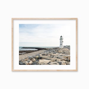 May include: A white lighthouse with a green roof stands on a rocky breakwater. The lighthouse is on a small island with a blue sky and ocean in the background.