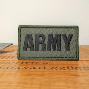 Peut inclure: Un écusson rectangulaire brodé vert olive portant le mot ARMY en lettres capitales noires épaisses. L'écusson présente une bordure cousue de couleur vert olive assortie et une base en tissu texturé pour fixation sur vêtements.