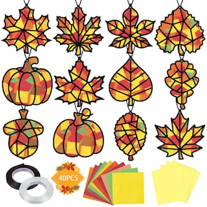 May include: A craft kit featuring eleven hanging decorations shaped like autumn leaves, pumpkins, and an acorn, each with a black frame and multicolored translucent panels. Includes two rolls of tape, a 40PCS label, and stacks of colored paper sheets.