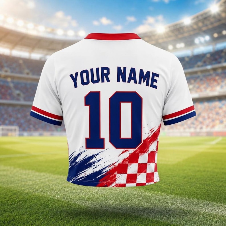 Pode incluir: Camisola de futebol branca com gola vermelha e detalhes azuis e vermelhos. A parte de tr&aacute;s apresenta o texto "YOUR NAME" acima do n&uacute;mero "10" em azul. A parte inferior tem um padr&atilde;o xadrez vermelho e branco e pinceladas azuis e vermelhas.