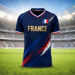 Puede incluir: Una camiseta de f&uacute;tbol azul marino con la palabra "FRANCE" en letras doradas en el pecho. La camiseta presenta la bandera francesa y detalles en rojo, blanco y azul. La camiseta tiene cuello en V y mangas cortas con ribetes rojos y blancos.