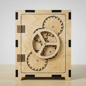 May include: A wooden safe with a light wood grain finish. The safe features a series of interlocking gears on the front, with a large central gear and smaller gears surrounding it. The safe has a rectangular shape with black accents.