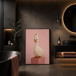 Pode incluir: Uma impressão de arte emoldurada apresentando um pato branco com pés e bico laranja, usando um rolo de papel higiênico na cabeça como um chapéu. O pato está sobre um cubo rosa contra um fundo rosa, apresentado em uma moldura preta.