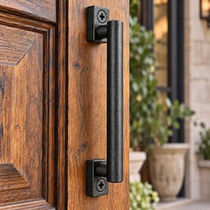 May include: A matte black cylindrical door handle with a textured finish, mounted vertically on a dark brown wooden door. The handle features two rectangular base plates, each secured with a single visible cross-head screw at the top and bottom.