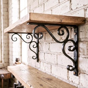 Può includere: Una mensola a muro composta da una spessa tavola di legno color naturale sostenuta da due staffe in metallo nero. Ogni staffa presenta un design decorativo a volute con dettagli metallici curvi, fissata alla parete con viti a vista.