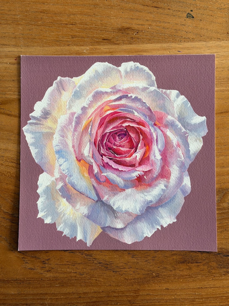 May include: A square art print featuring a detailed painting of a single rose. The flower has layered petals transitioning from deep magenta and pink at the centre to soft white and pale lavender at the edges, set against a solid mauve background.