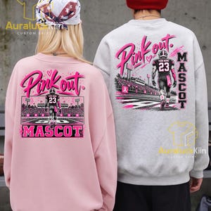 Puede incluir: Una sudadera rosa claro y una sudadera gris claro, ambas con un gr&aacute;fico en la espalda de un jugador de f&uacute;tbol americano en un campo con el texto Pink out. y MASCOT. La sudadera rosa se lleva con un pa&ntilde;uelo y la gris con un gorro de color rojo.