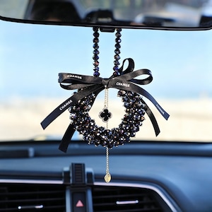 May include: A car rearview mirror hanging ornament featuring a horseshoe-shaped arrangement of dark, faceted beads. A black ribbon with the word CHANGE printed in white is tied at the top, and a gold-toned chain with a clover charm hangs below.