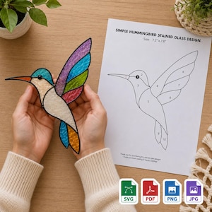 Könnte beinhalten: Ein Kolibri-Sonnenfänger aus Buntglas mit irisierenden violetten, blauen, grünen und orangefarbenen Flügeln und einem cremefarbenen Körper. Daneben liegt eine Papiervorlage mit der Aufschrift SIMPLE HUMMINGBIRD STAINED GLASS DESIGN, 18,3 cm x 19,8 cm.