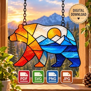 May include: A stained glass style bear suncatcher hanging by black chains. The bear features a geometric landscape with a yellow sun, blue mountains, and a red and orange gradient body. A digital download badge and file format icons are visible.