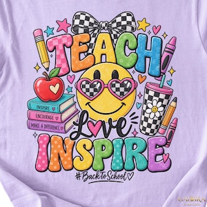 May include: A light purple t-shirt featuring a colorful graphic with the text TEACH, LOVE, INSPIRE, and #BackToSchool. The design includes a yellow smiley face with checkered heart sunglasses, a stack of books, an apple, a bow, and crayons.