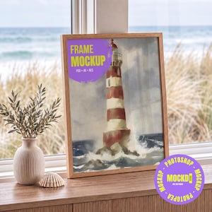 May include: A wooden picture frame containing a painting of a red and white striped lighthouse surrounded by crashing waves. The frame sits on a surface next to a white ribbed vase with a small plant and a seashell. Text reads FRAME MOCKUP.