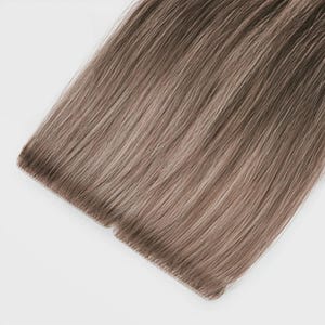 Op de afbeelding: Een recht haarverlengingsstuk met een mix van lichtbruine en asblonde tinten. Het haar is gerangschikt in een platte, uniforme rij met een versterkte bovenrand, wat een gladde, zijdeachtige textuur en een consistent, natuurlijk ogend kleurverloop laat zien.
