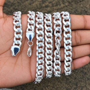 May include: A polished silver-tone curb chain necklace featuring thick, interlocking oval links. The chain includes a secure lobster claw clasp mechanism at one end and a smooth, flat metal end piece, showcasing a bright, reflective metallic finish.