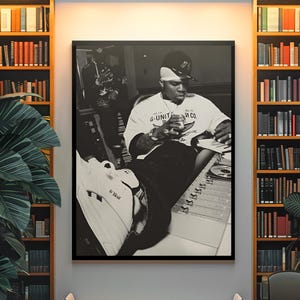 Pode incluir: Uma impressão de arte de parede emoldurada em preto e branco retratando uma pessoa usando um boné de beisebol e uma camiseta com o texto G-UNIT AND CO. A pessoa está sentada em uma mesa de som e usa tênis com o logotipo G-UNIT.