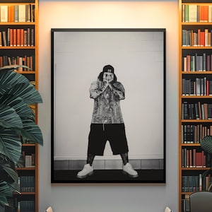 Könnte beinhalten: Ein schwarz-weiß gerahmter Wandkunstdruck, der eine Person mit einer Baseballkappe mit der Nummer 59, einem gemusterten T-Shirt und einer dunklen Shorts zeigt. Die Person steht mit den Händen vor dem Gesicht vor einer schlichten Wand.