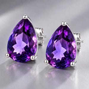 May include: A pair of stud earrings featuring large, pear-shaped, faceted purple amethyst gemstones set in polished silver-toned metal. Each earring is secured with a three-prong setting and includes a matching silver-toned metal post back.