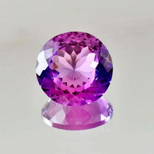 May include: A round, faceted gemstone with a vibrant purple and magenta colour gradient. The stone features a complex, symmetrical geometric cut that creates multiple light-reflecting surfaces, resulting in a brilliant, sparkling appearance.