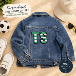 May include: A blue denim jacket for kids with the text "Personalised KIDS DENIM JACKET FOOTBALL INSPIRED INITIALS". The jacket has a green and white patch with the initials "TS". A soccer ball, white sneakers, a baseball cap, and sunglasses are also in the image.