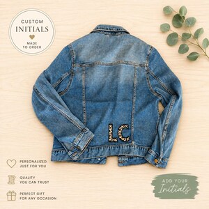 Puede incluir: Chaqueta vaquera azul claro con las iniciales "LC" en estampado de leopardo en la parte inferior de la espalda. La chaqueta tiene un diseño clásico con botones y bolsillos. La imagen incluye el texto "Custom Initials" y "Add Your Initials".