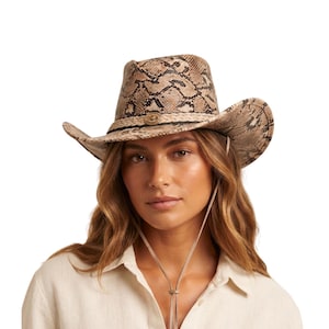 May include: A tan and brown snakeskin patterned cowboy hat featuring a pinched crown and a wide, curved brim. The hat is accented with a braided band and a central metallic circular concho detail, complete with a thin, adjustable chin strap.
