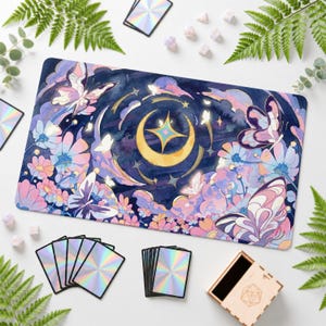 May include: A rectangular playmat featuring a dark blue night sky with a central yellow crescent moon and a four-pointed star. The design includes pink and blue flowers, several butterflies, and soft clouds. The mat is surrounded by holographic cards.