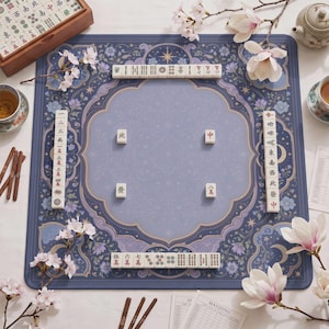 Può includere: Un tappetino da gioco per mahjong quadrato con un motivo floreale blu e viola e decorazioni celesti. Il tappetino è disposto con quattro file di tessere bianche da mahjong lungo i bordi e quattro tessere singole al centro.