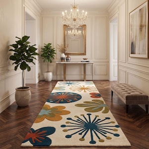 May include: A long rectangular area rug featuring a cream-colored background with a repeating pattern of stylized floral and starburst shapes in shades of deep blue, burnt orange, olive green, and light blue, arranged in a symmetrical layout.