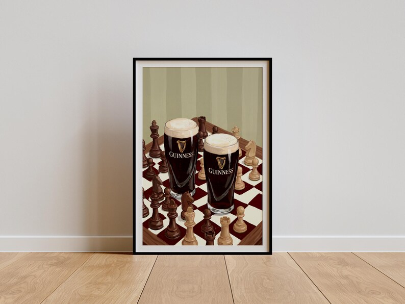 Peut inclure: Une impression d'art encadr&eacute;e repr&eacute;sentant deux verres de bi&egrave;re brune avec une mousse blanche cr&eacute;meuse, chacun portant le logo Guinness, plac&eacute;s sur un &eacute;chiquier &agrave; damier rouge et blanc entour&eacute; de diverses pi&egrave;ces d'&eacute;checs en bois clair et fonc&eacute;.