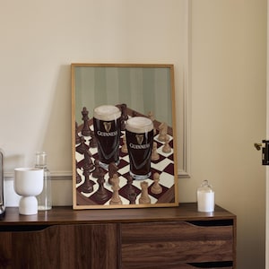 Peut inclure: Une impression d'art rectangulaire encadr&eacute;e repr&eacute;sentant un &eacute;chiquier avec des pi&egrave;ces en bois sombres et claires. Deux pintes de bi&egrave;re brune avec une mousse blanche cr&eacute;meuse, portant le logo Guinness, sont pos&eacute;es sur l'&eacute;chiquier.