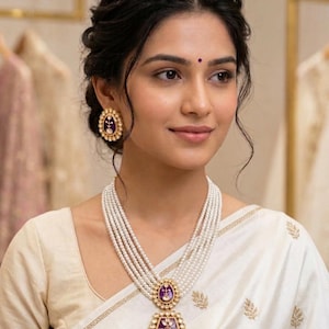 Peut inclure: Une femme porte un collier de perles et des boucles d'oreilles assorties. Le collier comporte plusieurs rangées de perles et un pendentif avec un centre violet et des accents dorés. Les boucles d'oreilles ont un design similaire. La femme porte un sari blanc.