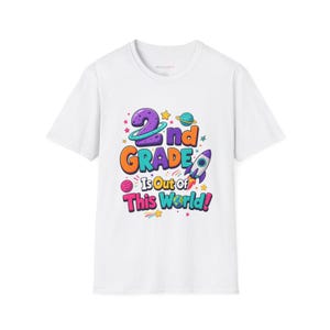 Puede incluir: Una camiseta blanca de manga corta con un gráfico colorido que incluye el texto 2nd GRADE Is Out of This World! El diseño presenta un número dos morado, un cohete, planetas, estrellas y una pequeña ilustración de la Tierra en colores vivos.