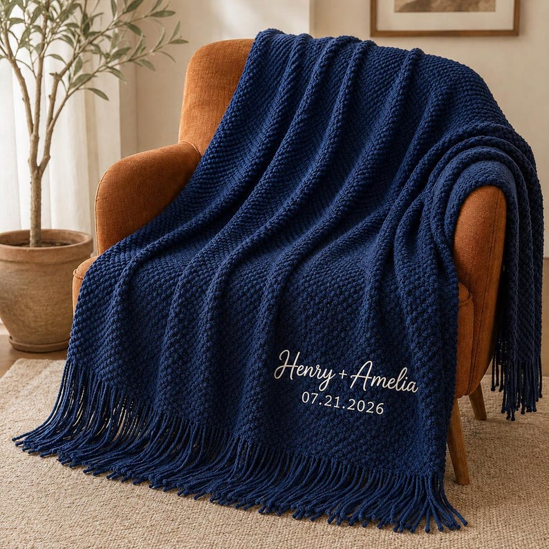 May include: A deep navy blue knitted throw blanket featuring a textured pattern and long fringe along the bottom edge. The blanket is embroidered with the white text Henry + Amelia and the date 07.21.2026 in a cursive and sans-serif font.