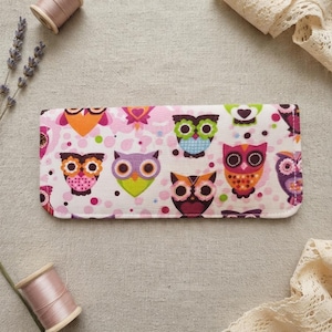 Op de afbeelding: Een rechthoekig stoffen etui met een herhalend patroon van kleurrijke uilen in tinten roze, oranje, paars, groen en bruin op een witte achtergrond met roze stippen. Het etui heeft afgeronde hoeken en een afwerking met gestikte randen.