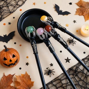 May include: Four wands with black shafts and silver-toned claw-shaped tops, each holding a different colored sphere: green, light pink, reddish-brown, and yellow. The claw designs feature intricate sword-like detailing on the handle base.