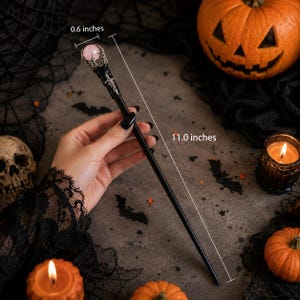May include: A black hair stick featuring a silver-toned claw setting that holds a round, pale pink stone at the top. The total length of the hair stick is 11.0 inches, and the diameter of the pink stone is 0.6 inches as indicated by labels.