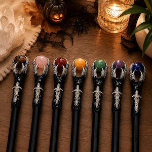 May include: Seven black wands arranged in a row, each featuring a silver-toned metal claw clutching a spherical gemstone. The gemstones are tiger's eye, rose quartz, carnelian, yellow jade, green aventurine, amethyst, and blue lapis lazuli.