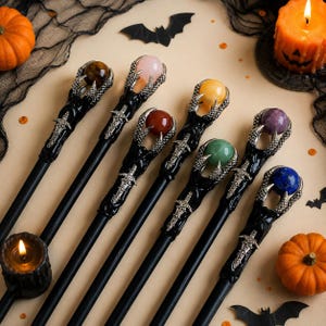 May include: A collection of six black wands, each featuring a silver-toned metal handle shaped like a sword and a claw-like topper holding a polished gemstone sphere. The stones include tiger's eye, rose quartz, carnelian, yellow jade, green aventurine, and lapis lazuli.