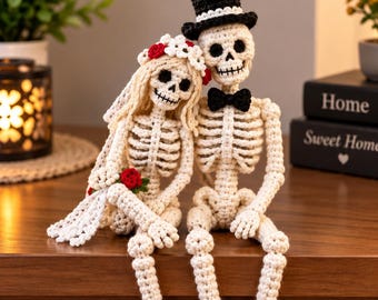 May include: Two crocheted skeleton figures sitting side by side. The figure on the left wears a white floral crown with red accents and a white veil. The figure on the right wears a black top hat with a white band and a black bow tie.