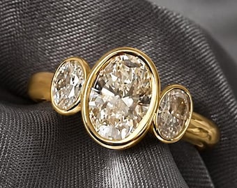 May include: A gold ring featuring a large central oval-cut stone flanked by two smaller oval-cut stones. Each stone is secured in a smooth, polished gold bezel setting. The band is crafted from solid yellow gold with a rounded, polished finish.