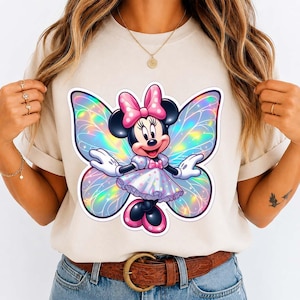May include: A beige t-shirt featuring a Minnie Mouse graphic with iridescent butterfly wings. Minnie Mouse is wearing a pink bow, dress, and shoes. The graphic is centered on the shirt.