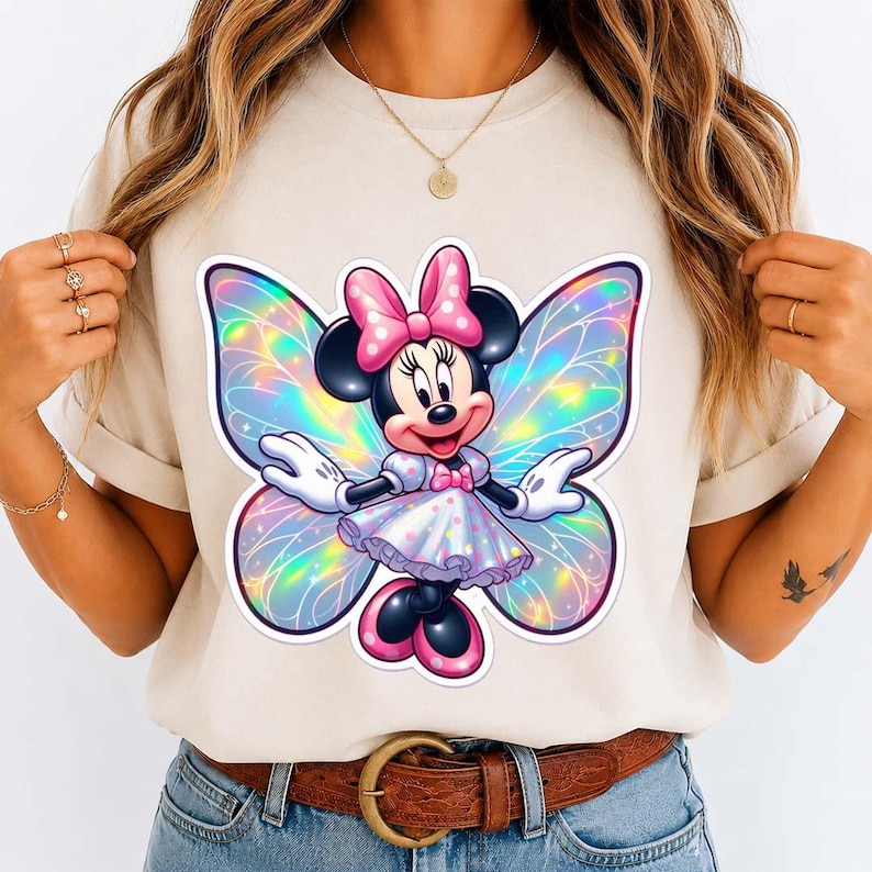 May include: A beige t-shirt featuring a Minnie Mouse graphic with iridescent butterfly wings. Minnie Mouse is wearing a pink bow, dress, and shoes. The graphic is centered on the shirt.