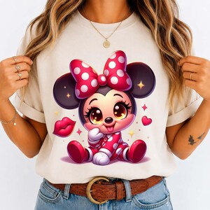 May include: A beige t-shirt featuring a cartoon illustration of a baby mouse character. The mouse wears a red and white polka dot outfit and bow. The design includes hearts and a pair of red lips.