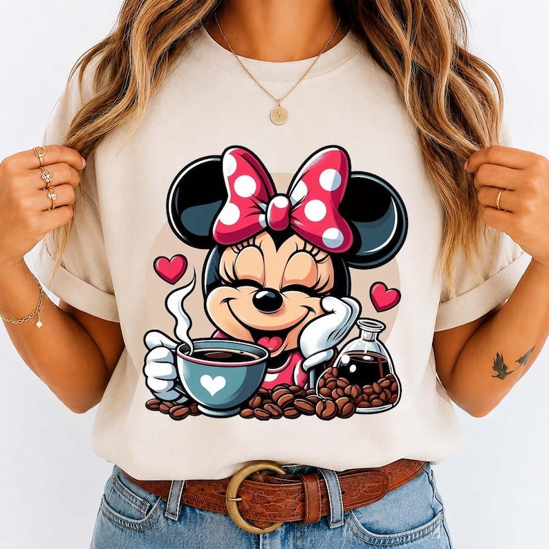 May include: A beige t-shirt featuring a cartoon Minnie Mouse with a red and white polka dot bow, holding a coffee cup with a heart design. Coffee beans and a glass carafe are also present.