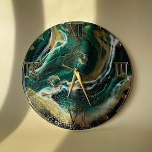 Könnte beinhalten: Eine runde Wanduhr mit einem wirbelnden, smaragdgrünen, schwarzen und goldenen Marmormuster und glänzender Oberfläche. Das Zifferblatt zeigt goldene römische Ziffern an den Positionen zwölf, drei, sechs und neun Uhr sowie goldene Zeiger.