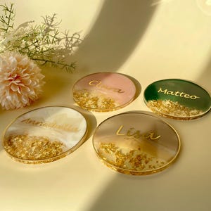 Può includere: Quattro sottobicchieri personalizzati in resina con dettagli in foglia d'oro. Ogni sottobicchiere presenta un nome diverso in oro: Annabella, Clara, Lisa e Matteo. I sottobicchieri sono in tonalità rosa, verde e neutre.
