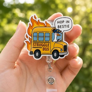 Può includere: Un portabadge raffigurante uno scuolabus giallo avvolto da fiamme arancioni. Un'oca bianca con un berretto blu guida l'autobus, etichettato STRUGGLE BUS. Un fumetto sopra l'autobus contiene il testo nero HOP IN BESTIE.